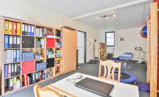 Behandlungsraum mit Schreibtisch und Bücherregalen bei Ergomed, Praxis für Ergotherapie und Logopädie in Hamburg Heimfeld
