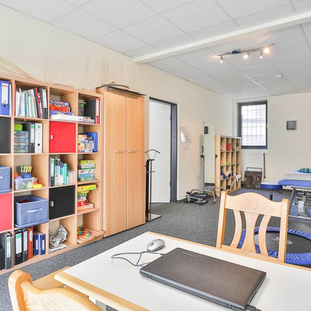 Behandlungsraum mit Schreibtisch und Bücherregalen bei Ergomed, Praxis für Ergotherapie und Logopädie in Hamburg Heimfeld